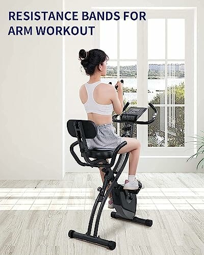 Woman using resistance bands on exercise bike indoors.