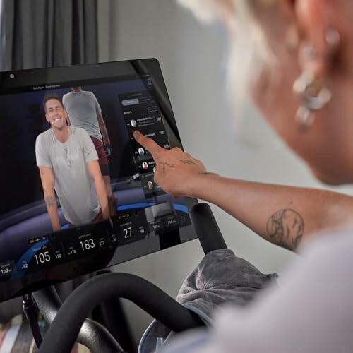 Person interacting with a fitness bike touchscreen display showing a virtual instructor.